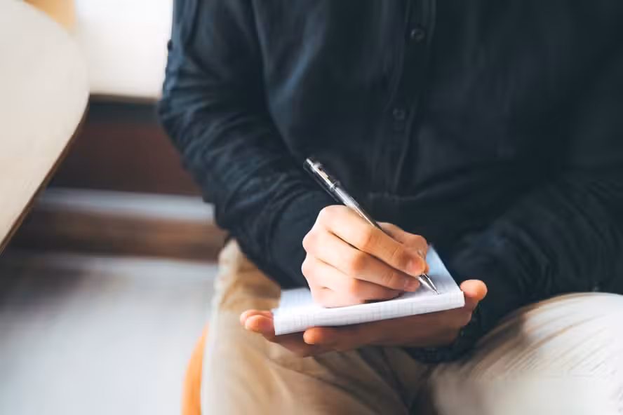 Pessoa escrevendo manualmente em um bloco de notas de papel.